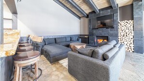 A modern outdoor living area with a stone fireplace, built-in TV, and comfortable seating.