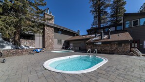 A pool area with two hot tubs, stone walls, and a large tree.