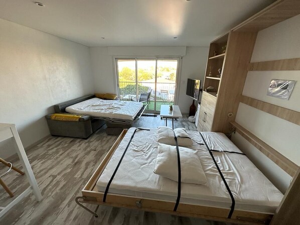 A modern room with two beds, a small table, a TV, and a balcony with a view. - Large studio in Fréjus (FREJUS)