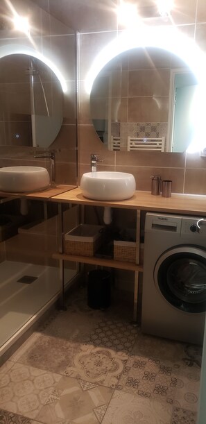 A bathroom with two sinks, a mirror, a shower, and a washing machine.