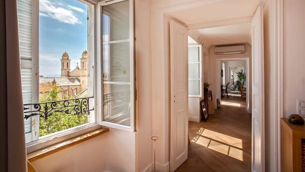 A corridor with a view of a church through an open window. - Le Saint-Jean (Bastia)