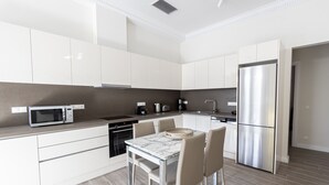 Cozinha moderna com armários brancos, eletrodomésticos de aço inoxidável e bancada de mármore.