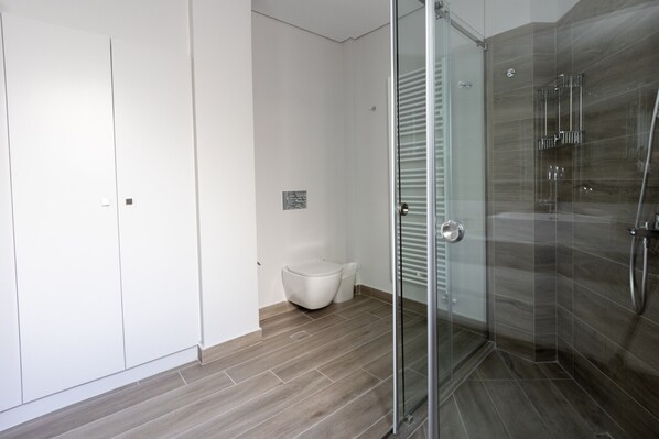 A modern bathroom with a glass shower enclosure, a toilet, and a white cabinet. - Ancient Athens Great Apt Home Office w/Acropolis View (Athens)