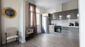 A modern kitchen with stainless steel appliances, a dining area with a chair, and a wall clock. - Plaka's Privileged Accommodation (Athens)
