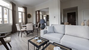 A spacious living room with a light-colored sofa, a dining area with chairs, a coffee table, and a lamp. - Plaka's Privileged Accommodation (Athens)