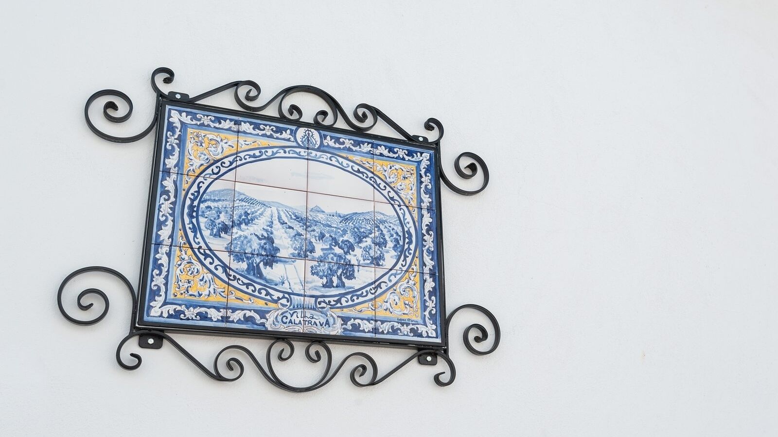 A decorative tile with a landscape scene, mounted on a wall with a black metal frame.