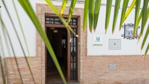 A brick building entrance with a wooden door, a sign for 'Vivienda Rural Villa Calatrava', and a power outlet on the wall. - Alojamiento Rural Villa Calatrava Santiago de Calatrava by Ruralidays (Jaén)