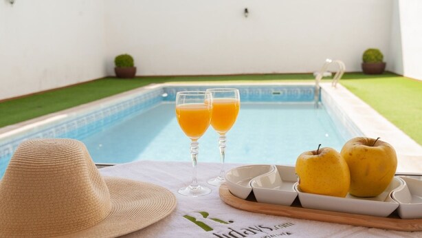 A poolside setting with two glasses of orange juice, a straw hat, and two apples on a tray. - Alojamiento Rural Villa Calatrava Santiago de Calatrava by Ruralidays (Jaén)