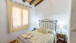 Une chambre à coucher avec un lit, deux tables de chevet, une fenêtre avec des rideaux et un plafond en bois.