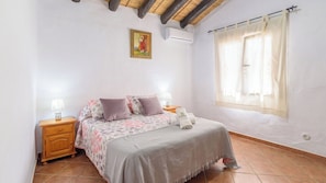 Quarto com cama, mesas de cabeceira, janela com cortinas e ar-condicionado fixado na parede.