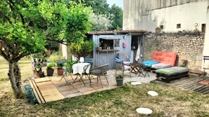 A rustic outdoor seating area with a wooden deck, a small bar, and a stone wall. - A quiet little oasis, 5 km from the port of La Rochelle (Dompierre-sur-Mer)