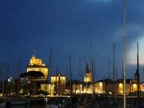 A marina with several boats docked, a prominent building with illuminated windows, and a clear sky. - A quiet little oasis, 5 km from the port of La Rochelle (Dompierre-sur-Mer)