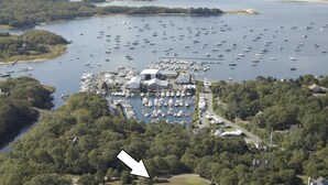 An aerial view of a marina with numerous boats docked, surrounded by dense forest. - Nestled in Cataumet, One of the Cape’s Hidden Gems (Bourne)
