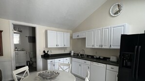 A kitchen with white cabinets, a black refrigerator, a ceiling fan, and a dining table with chairs. - Nestled in Cataumet, One of the Cape’s Hidden Gems (Bourne)