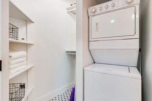 A laundry room with stacked washing machines, shelves with folded towels, and a mop on the floor.