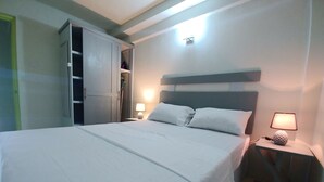 Ein ordentlich bezogenes Bett mit weißen Laken, eine Nachttischlampe und ein teilweise geöffnete Kleiderschrank.