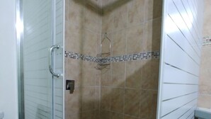 Eine gläserne Dusche mit gefliestem Boden und einem Metallregal.