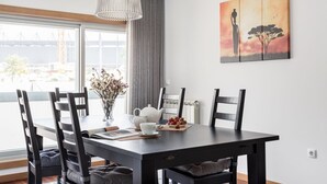 Un comedor con una mesa, sillas, un florero con flores, una tetera y un cuadro en la pared.