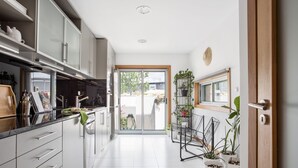 Una cocina moderna con armarios blancos, encimera negra y puerta corredera de vidrio que da a un balcón.