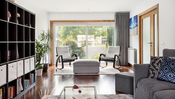 Una sala de estar moderna con un ventanal grande, una estantería, dos sillones, un sofá y una mesa de centro.