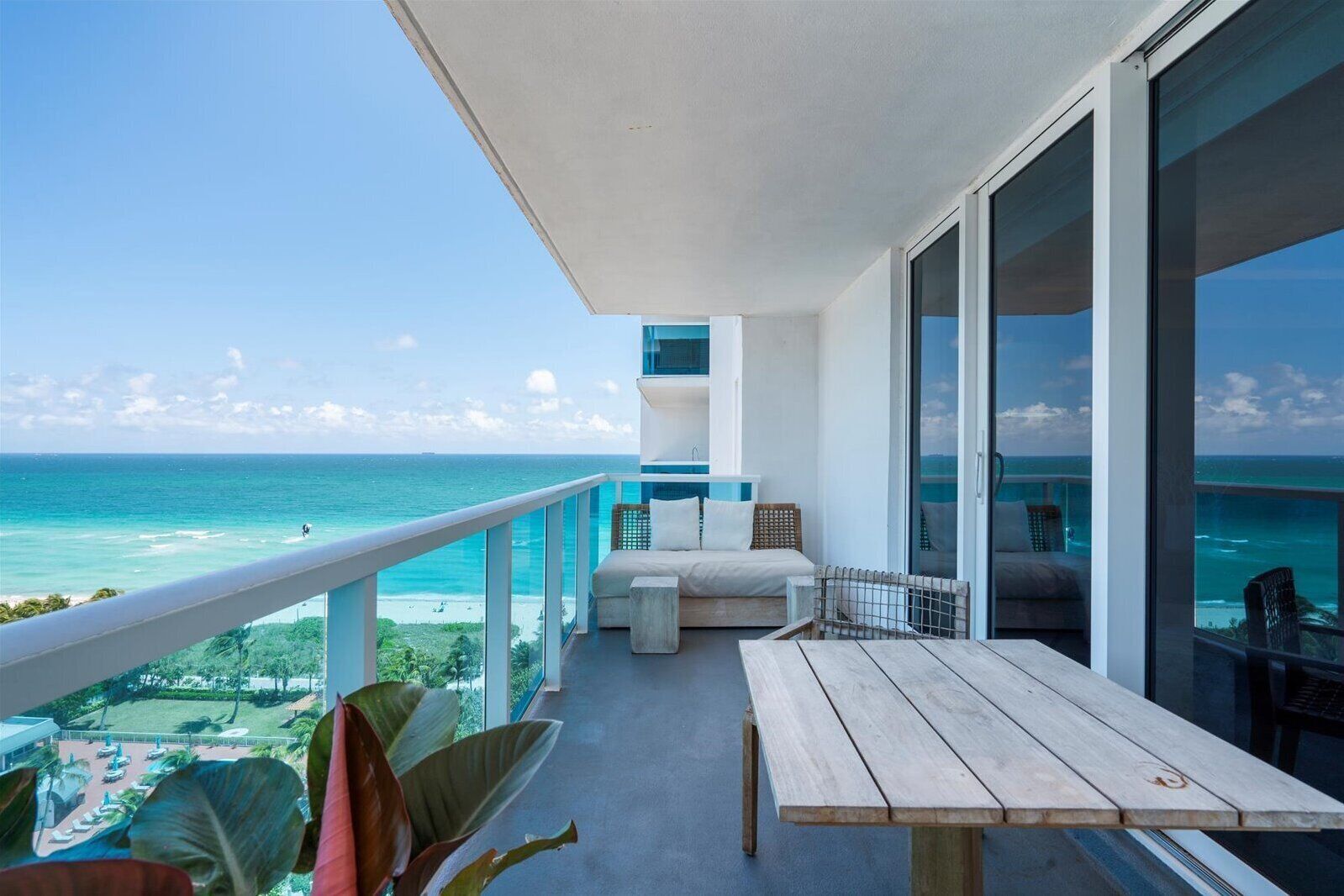 Un balcón con mesa y sillas de madera, con vistas a la playa y el océano.