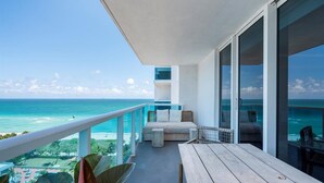 A balcony with a wooden table and seating, overlooking a beach and ocean. - Luxurious 3/3 Ocean View Condo 1413 - Located at 1 Hotel & Homes South Beach (Miami Beach)