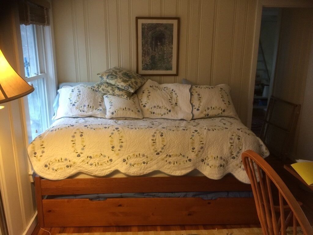 Una camera da letto con un letto di legno, una coperta e un quadro appeso al muro.