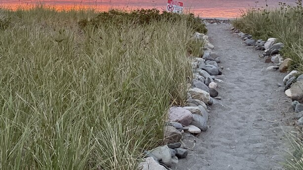Een pad dat naar een strand leidt, met uitzicht op een zonsondergang.