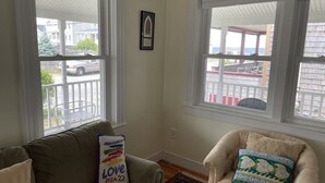 Een woonkamer met twee ramen, een bank, een fauteuil en een vloerkleed.