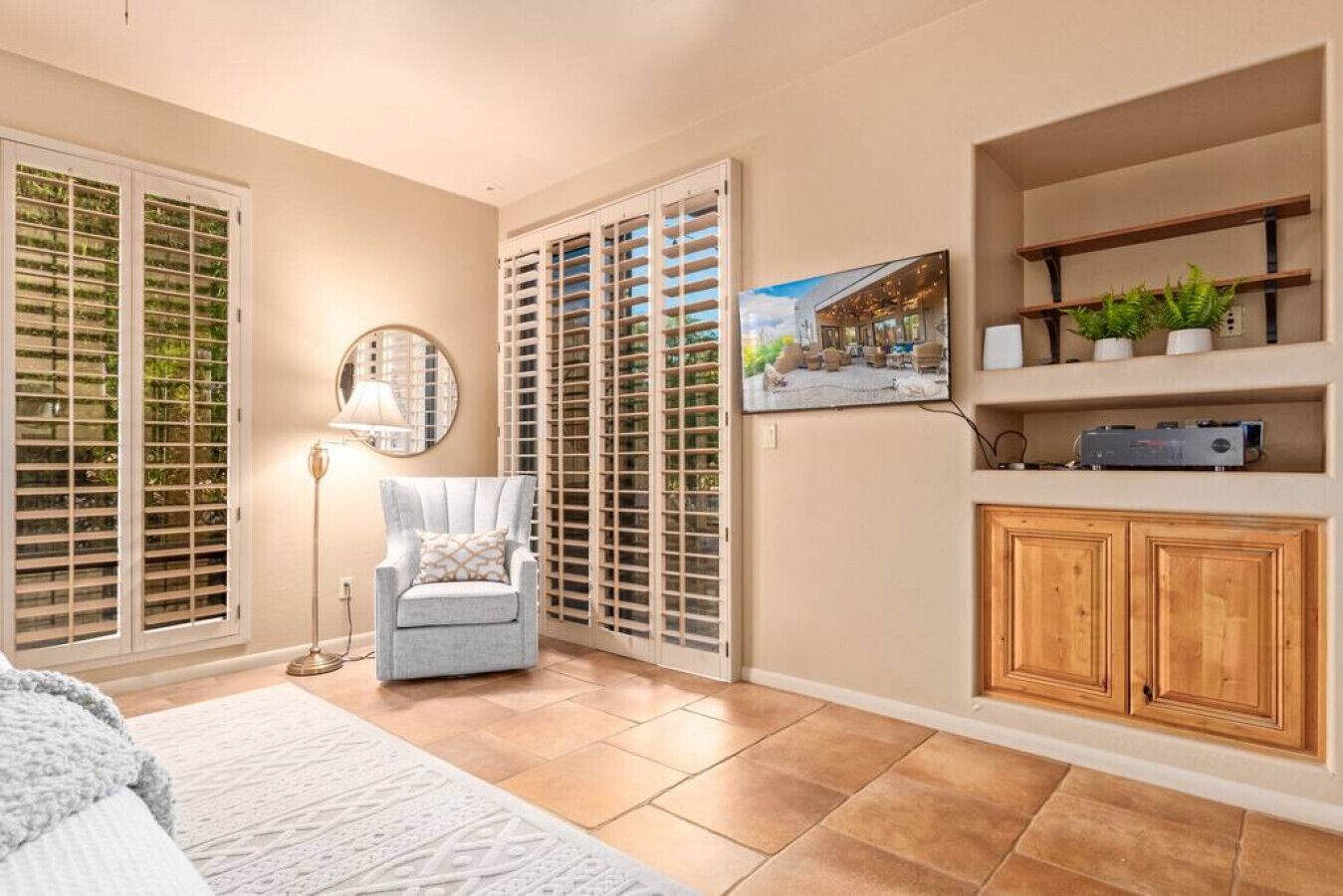 A room with a chair, a lamp, a TV, a cabinet, and a window with blinds.