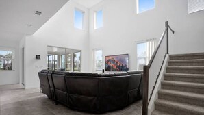Amplia sala de estar con un sofá de cuero negro y gran capacidad, una escalera y un ventanal que ofrece luz natural.