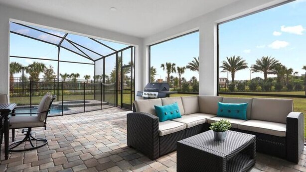 Un patio cubierto con una zona de estar, una parrilla y vistas a palmeras.