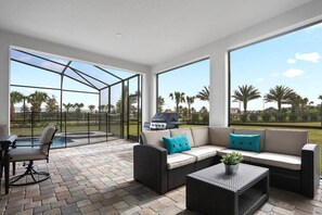 A covered patio area with a seating arrangement, a grill, and a view of palm trees. - Beautiful, Comfortable home by Disney!! (Four Corners)