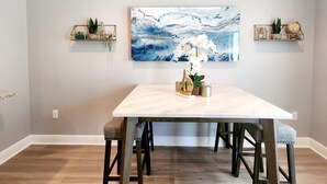 Een eetruimte met een marmeren tafel, twee stoelen, een schilderij en twee zwevende planken met planten en decoratieve objecten.