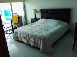 A bedroom with a bed, a nightstand, a lamp, and a chair.