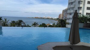 En swimmingpool med utsikt över havet och byggnader i bakgrunden.