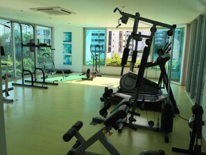 A spacious gym with various exercise equipment, large windows offering views of the city, and a clean, modern interior.