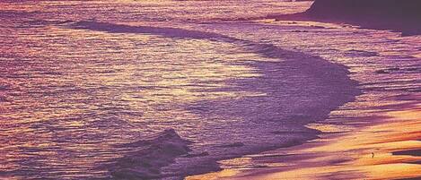 A sunset over a beach with waves and a pier in the distance.