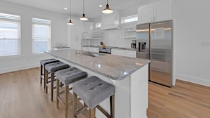 Una cocina moderna con una isla central, taburetes de bar, electrodomésticos de acero inoxidable e iluminación colgante.