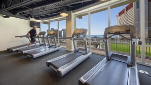 Ein Fitnessstudio mit Laufbändern, Kraftgeräten und großen Fenstern mit Blick auf eine Skyline.