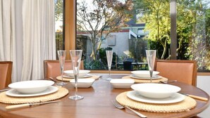 Une table à manger dressée pour six personnes, avec des assiettes blanches, des verres transparents et des sets de table en fibres tressées.