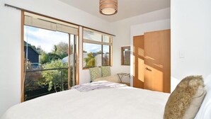Une chambre avec un grand lit, une fenêtre avec des stores, une porte en bois et une vue sur la verdure.