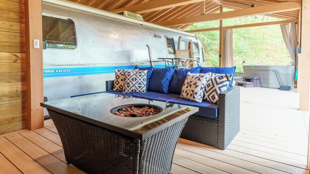Un espacio al aire libre cubierto con una mesa de comedor, mobiliario de mimbre y una caravana.