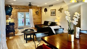 Una camera accogliente in stile baita di legno, con zona pranzo, pavimenti in legno, ventilatore a soffitto e una testa di cervo appesa al muro.