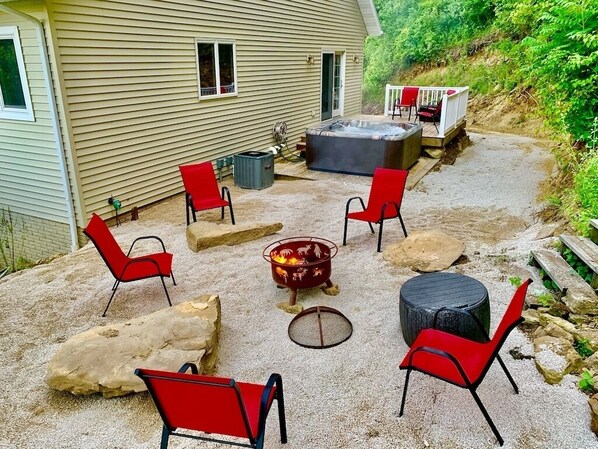 An outdoor patio with a hot tub, red chairs, and a fire pit.