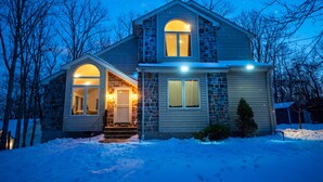 Ett tvåvåningshus med en fasad av sten, ett stort, välvt fönster och en snötäckt trädgård framför huset.