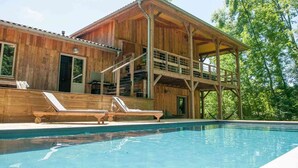 A wooden cabin with a pool, a balcony, and a covered outdoor seating area.