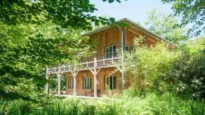 A wooden cabin with a balcony, surrounded by lush greenery.