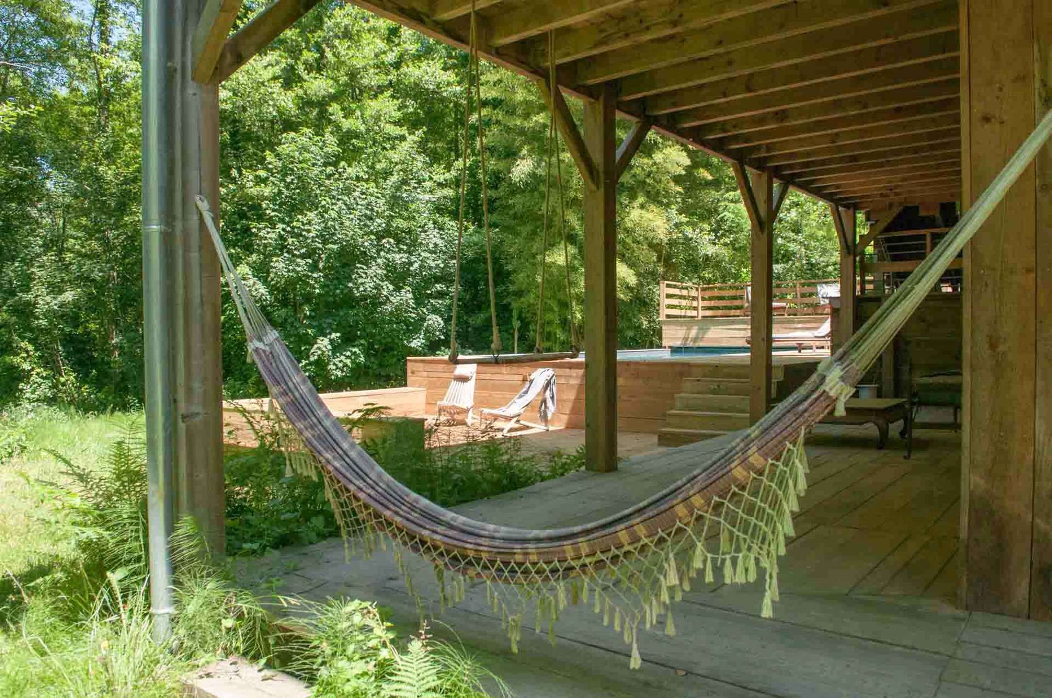 A hammock under a wooden pergola in a lush garden setting.