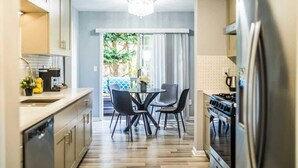 Une cuisine moderne avec un coin repas, agrémentée d’un lustre, d’un réfrigérateur et offrant une vue sur l’extérieur.